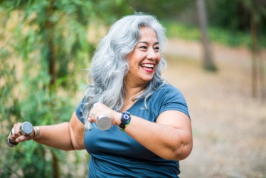 Older Hispanic Woman Happily Lifts Small Dumbbells