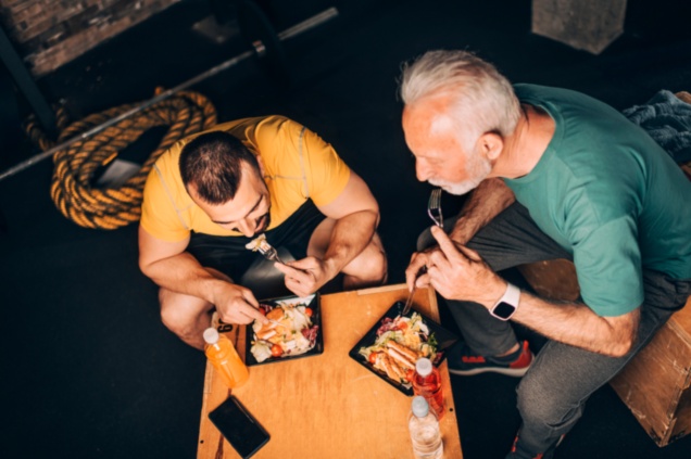 Older White Man and Trainer Eat High Protein Meals at Gym